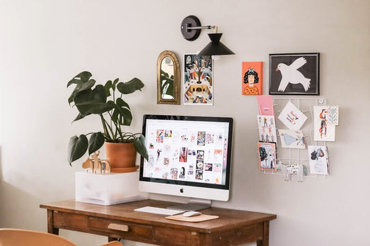 Home office desk with a computer, plant, and quirky wall art, ideal for setting up lighthearted practical jokes in the workplace.